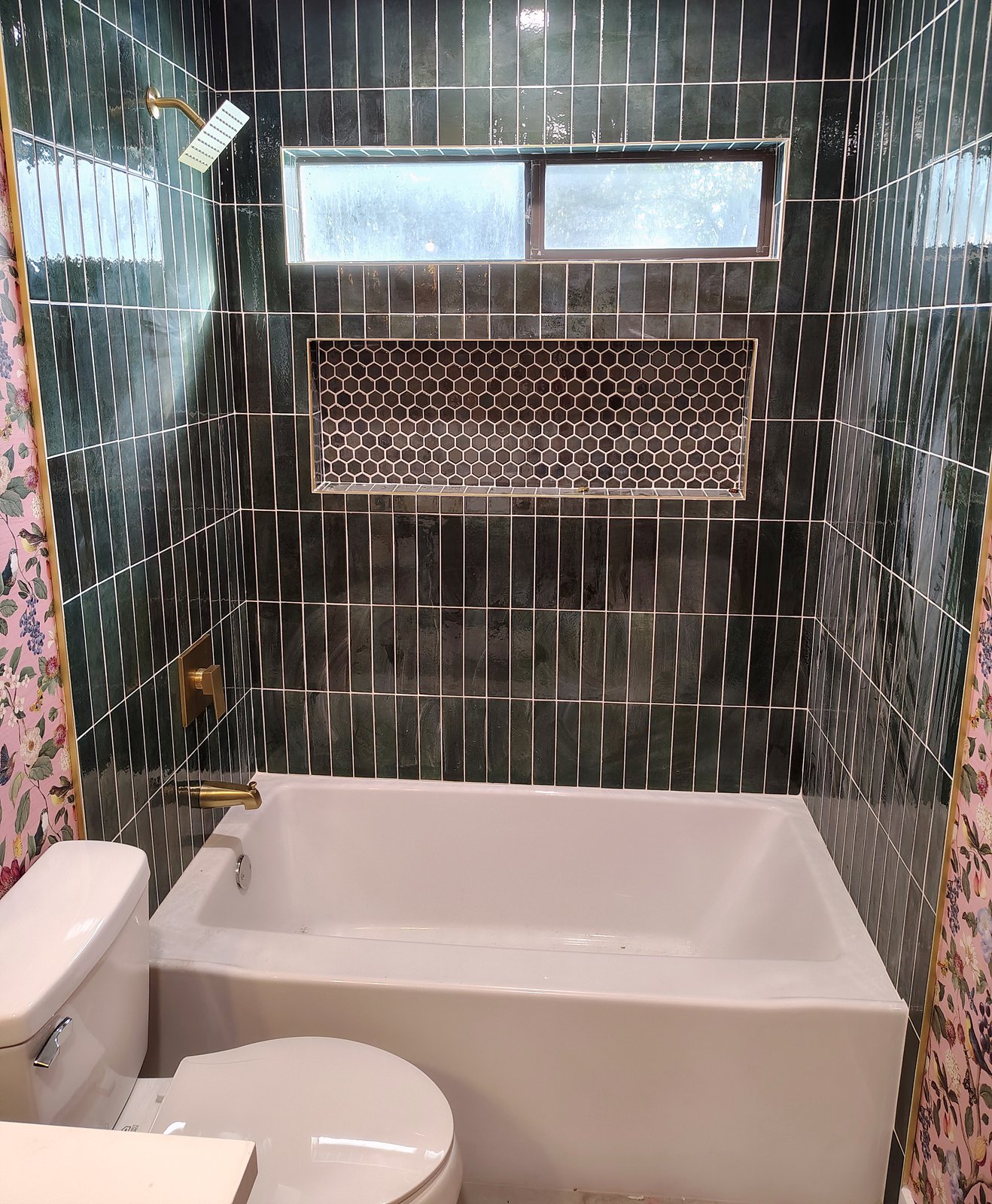 Tub and shower with deep-green vertical stacked tile, a hexagon-tile niche, a window and brushed-gold fixtures.