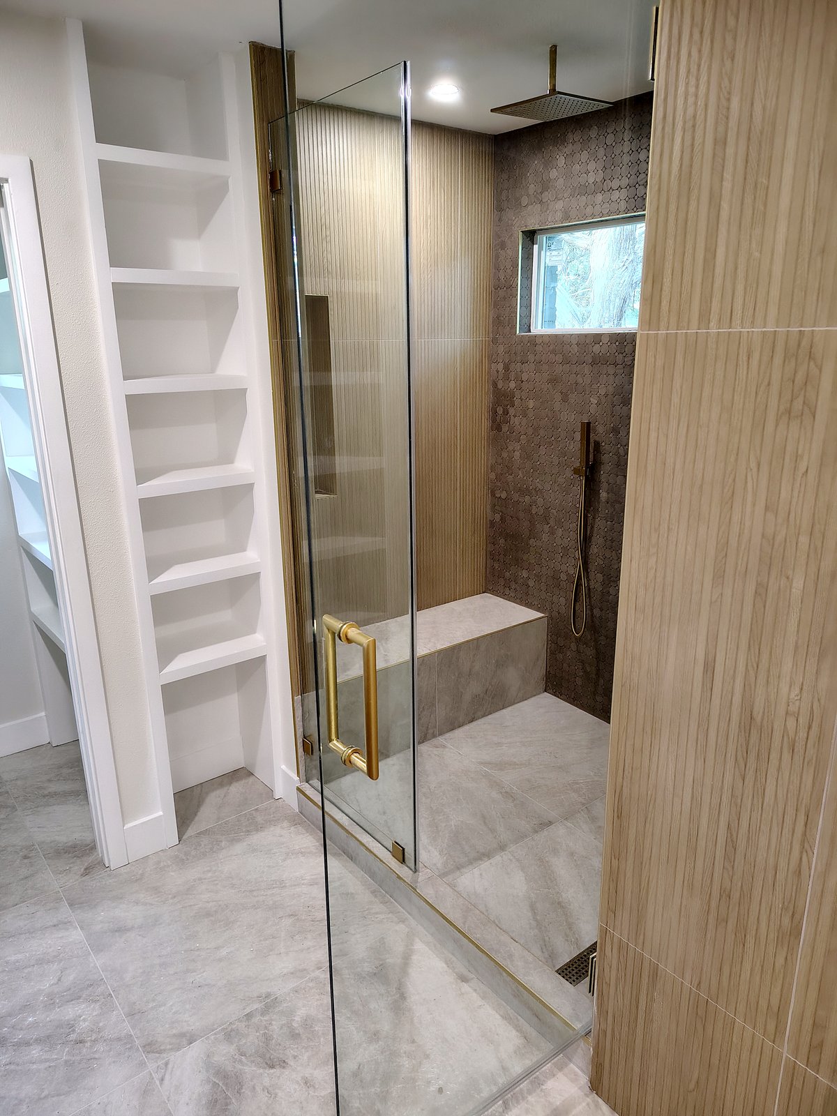 Frameless glass shower beside built-in white closet shelving in a remodeled primary bath.