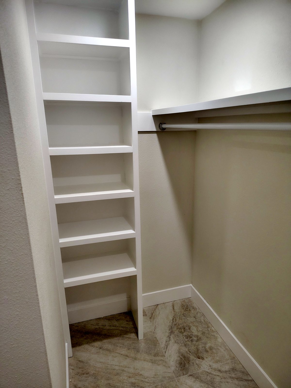 Walk-in closet with a floor-to-ceiling white shelf tower, a hanging rod and a shelf.